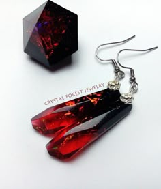 two red and black earrings sitting next to each other on a white surface with the words crystal forest jewelry written below them