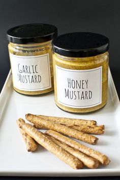 two jars of honey mustard sit on a white plate next to some cinnamon stick sticks