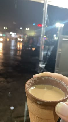 someone holding up a cup of coffee in front of a parking lot at night time