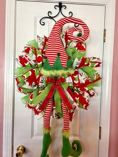 a christmas wreath hanging on the front door with green and red ribbons, elf feet and bell