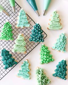 cookies decorated with icing and christmas trees on a cooling rack, next to pens