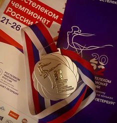 an olympic medal is laying on top of a book with ribbon around it and another award in the background