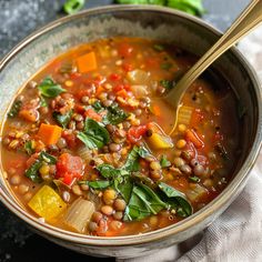 a bowl filled with soup and vegetables on top of a white cloth next to a spoon