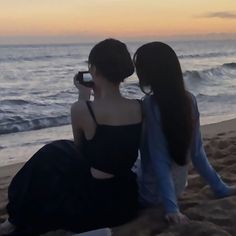 two women sitting on the beach looking at the ocean