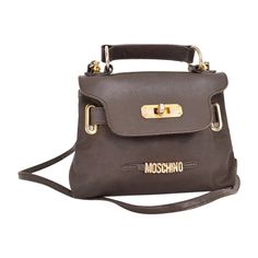 A Chic and Fun Vintage 1990's Moschino brown nylon miniature 'Kelly' bag with gold tone metal hardware and leather features. Features: Detacheable shoulder strap Belt loop option Top handle MOSCHINO Gold Tone Metal lettering Made In Italy Measurements: 2'' Width x 5'' Depth x 7'' Length Strap: 48'' Condition: 7/10 Some tarnishing to the hardware and signs of general usage. Moschino Vintage, Metal Lettering, Micro Bag, Kelly Bag, Metal Letters, Metal Hardware, Vintage Jewellery, Gold Tone Metal, Fashion Handbags