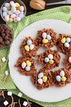 a white plate topped with cookies covered in chocolate eggs and mini eggs next to small bowls of candy