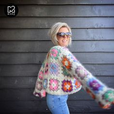 a woman with blonde hair and sunglasses is wearing a colorful knitted sweater while standing in front of a black wall