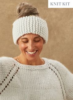 a smiling woman wearing a knitted headband and holding a cell phone in her hand