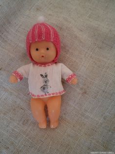 a small doll with pink hair wearing a sweater and knitted hat on the floor