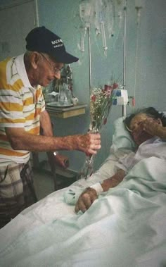 an old man in a hospital bed with flowers on his hand and another person laying down next to him