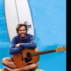 a man sitting in front of a surfboard holding a guitar