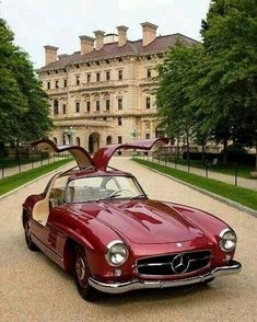 an old red car parked in front of a large building with its open hood up