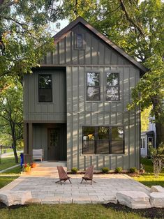 two lawn chairs sitting in front of a gray house with trees and grass around it