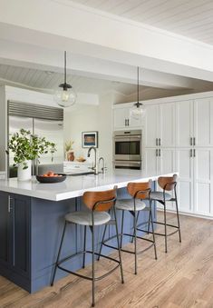 a kitchen island with four stools and an oven in the center, surrounded by white cabinets