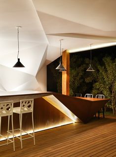 an outdoor bar with three stools next to it and lights hanging from the ceiling