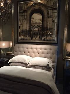 a bed with white linens and pillows in a dark room next to a chandelier