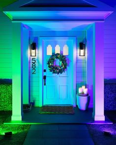 the front door is lit up with purple and green lights, wreaths and candles