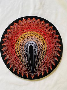 a black plate with red, yellow and orange string art on the front is an image of a person's head