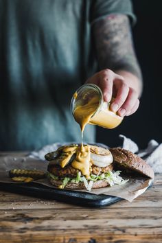 a person pouring mustard on top of a burger