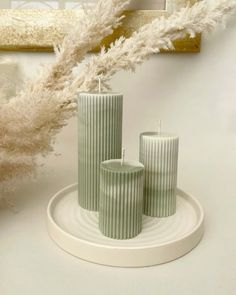 three green candles sitting on top of a white plate next to some pamodia