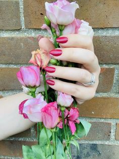 a woman's hand with pink and white flowers in front of a brick wall