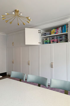 a dining room table with blue chairs in front of white cabinets and cupboards behind it