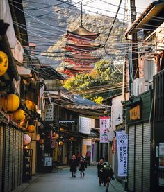 people walking down an alley way with many buildings in the back ground and mountains in the background