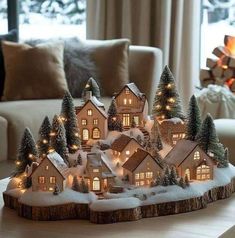 a lit up christmas village on a table in front of a living room with a fireplace