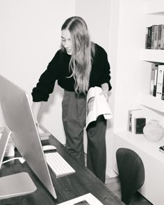 a woman standing in front of a computer on top of a wooden desk next to a bookshelf