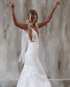 a woman in a wedding dress is dancing with her arms up and hands behind her head