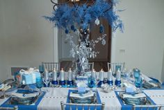 a dining room table set with blue and silver place settings, centerpieces and napkins