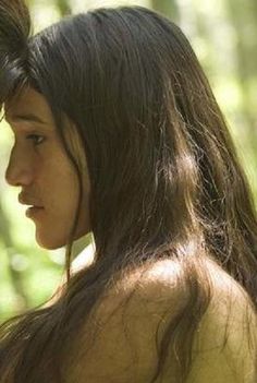 a young man and woman standing next to each other in the woods looking at each other