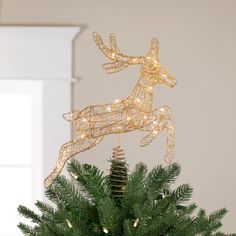 a christmas tree decorated with lights and a reindeer figure on top of it in front of a window