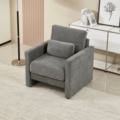 a gray chair sitting on top of a white floor next to a table and lamp