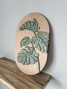 a wooden plaque with leaves on it sitting on top of a wood shelf next to a wall