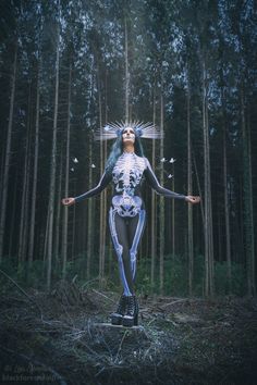 a woman standing in the middle of a forest with her arms spread out and two birds flying over her head