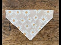 a dog bandana with daisies on it sitting on a wooden floor in front of a wood table