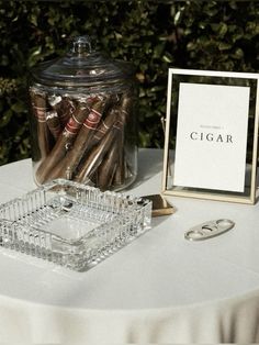 a glass jar with cigars in it sitting on top of a white table cloth