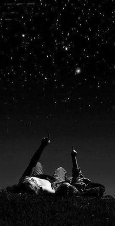 two people laying on the ground under stars in the night sky with their hands up