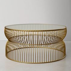 two round glass coffee tables with gold metal frames on the top and bottom, sitting side by side in front of a white wall