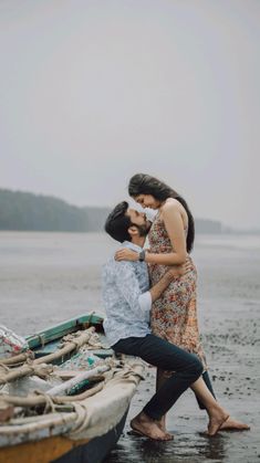 two people standing next to each other near a boat on the beach, with one person touching the woman's face