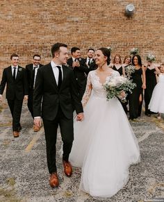 a bride and groom are walking in front of their wedding party