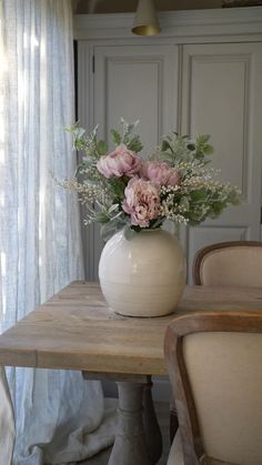 a white vase filled with flowers sitting on top of a wooden table next to two chairs