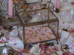 a glass box filled with jewelry on top of a table next to candles and other items