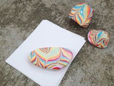 three colorful rocks sitting on top of a piece of white paper next to each other