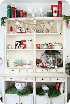 a white hutch filled with lots of christmas decorations and dishes on top of it