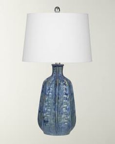 a blue vase lamp with a white shade on the base and a light in front of it