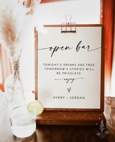 an open bar sign sitting on top of a wooden table next to a vase filled with flowers