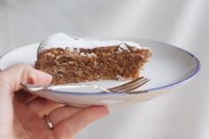 a hand holding a plate with a piece of cake on it and a fork in it