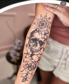 a woman's arm with a skull and flowers tattoo on her left arm,